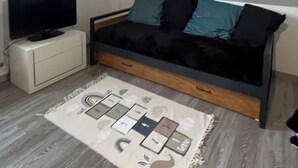 A small, modern bedroom with a sloped ceiling, a bed with teal and black bedding, a TV on a white dresser, and a patterned rug on the floor.