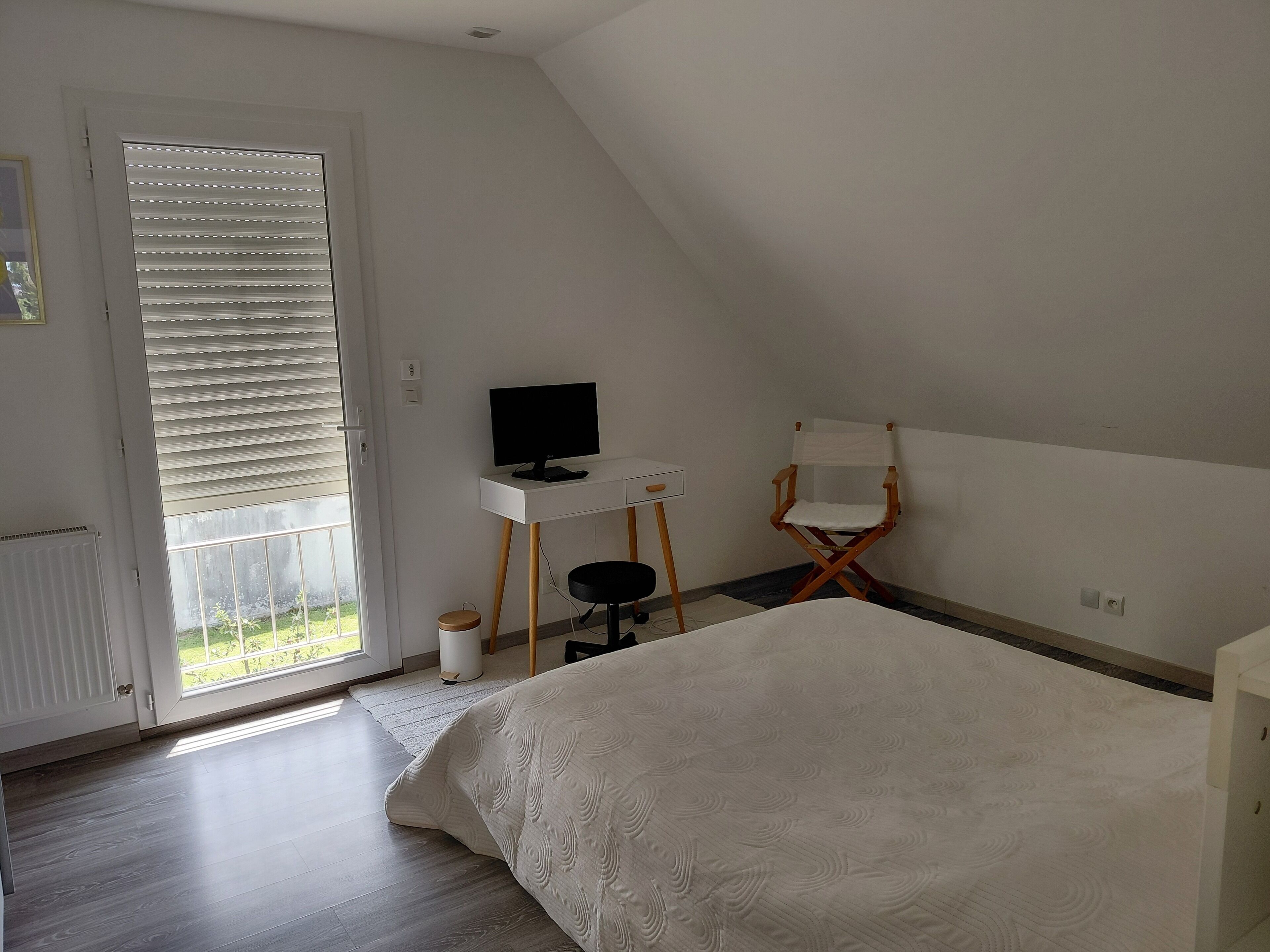 Um quarto com cama, escrivaninha com computador, cadeira e janela com persianas.