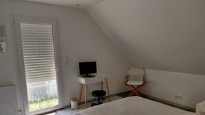 A bedroom with a bed, a desk with a computer, a chair, and a window with blinds.