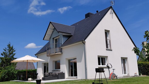 A modern two-story house with a balcony, a barbecue grill, and outdoor seating.