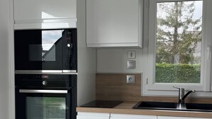 A modern kitchen with white cabinetry, a built-in oven, a microwave, and a window with a view of trees.