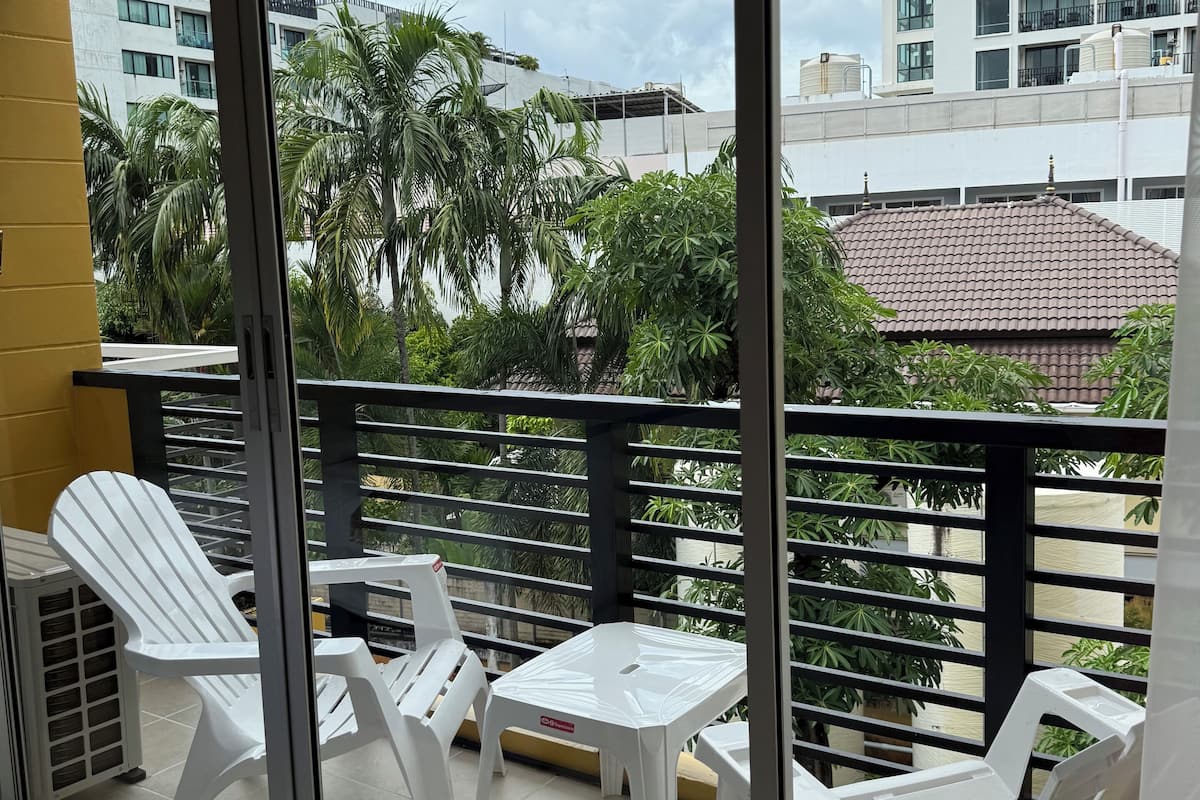 Uma varanda com cadeiras de plástico branco e uma pequena mesa, com vista para uma paisagem urbana com edifícios e palmeiras.