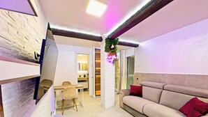 Un salon moderne avec un canapé beige, une table à manger et un téléviseur fixé au mur, qui est en briques.