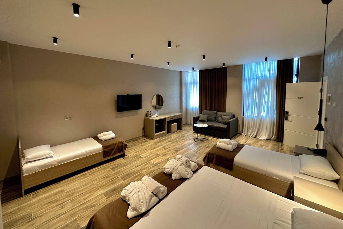 A hotel room with two single beds, a sofa, a desk, a TV, and a wardrobe.