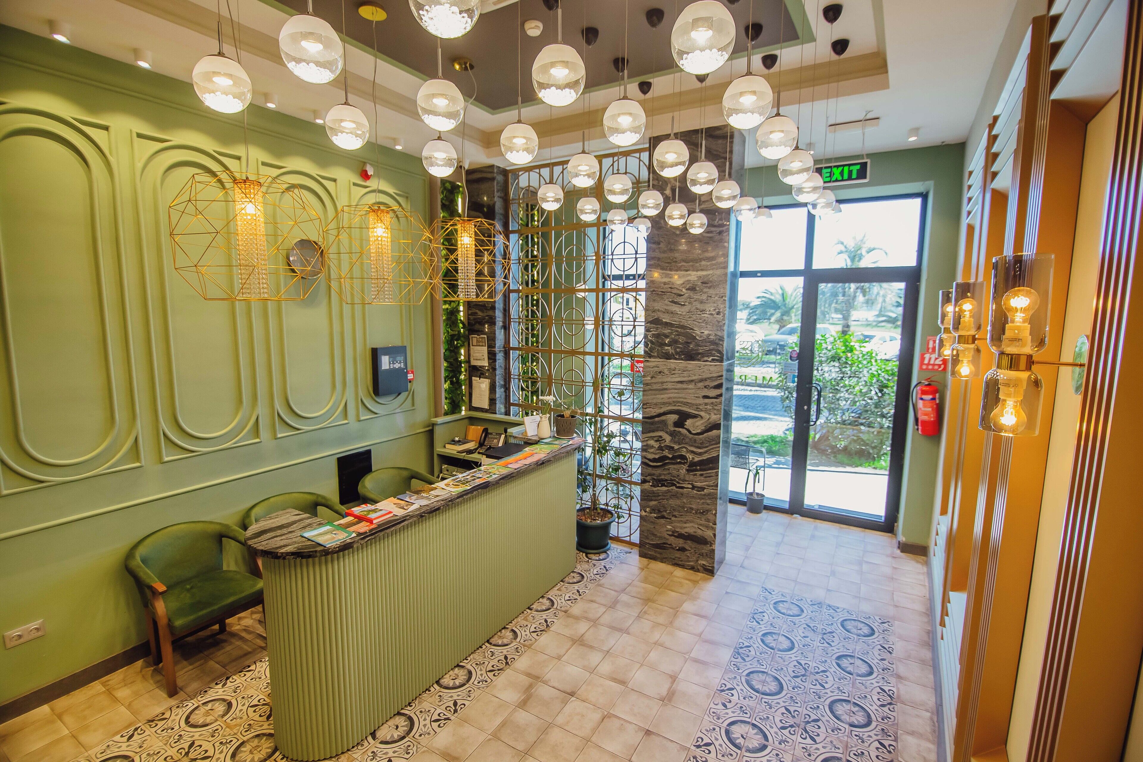 A reception area with a green counter, multiple hanging light fixtures, and a view of the outdoors through a glass door.