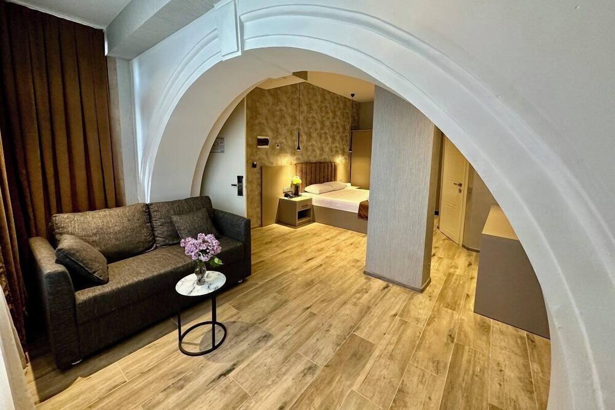 A modern living room with a sofa, a small round table with a vase, and a wooden floor.