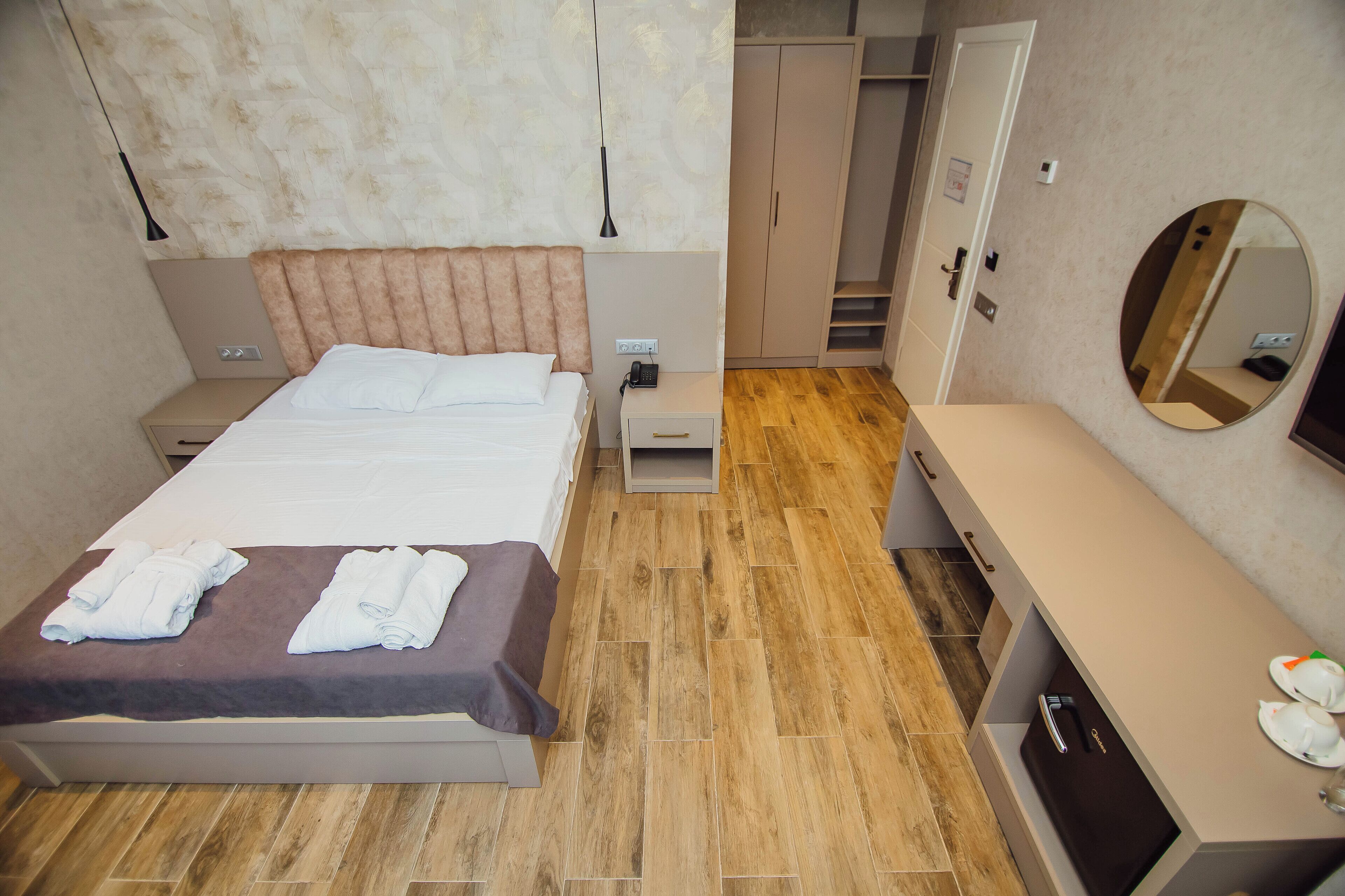 Quarto de hotel com cama, mesas de cabeceira, guarda-roupa, espelho e secretária com cadeira.