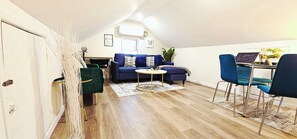 Ein kompakter Wohnbereich mit einem blauen Sofa, einem runden Couchtisch und einem Essbereich mit Stühlen.