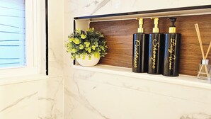 Ein Badezimmerschrank mit einer Topfpflanze, drei schwarzen Flaschen mit goldenen Verschlusskappen und einem Reed-Diffusor.
