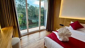 A hotel room with a large sliding glass door leading to a balcony, a bed with a red blanket and a decorative pillow, and a wooden nightstand. - ZAAD SUITE (Meenachil)