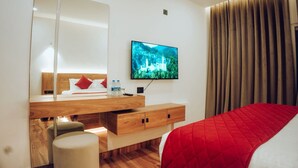 A modern hotel room with a wooden desk, a large mirror, a flat-screen TV, and a bed with a red quilt. - ZAAD SUITE (Meenachil)