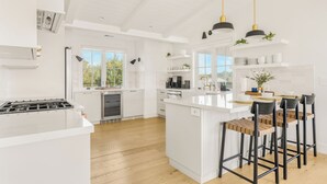 A modern kitchen with white cabinetry, a central island with bar stools, and pendant lighting. - Vineyard Views w/ Pool & Game Room Near Trails | Beginnings Ranch & Vineyard (Paso Robles)