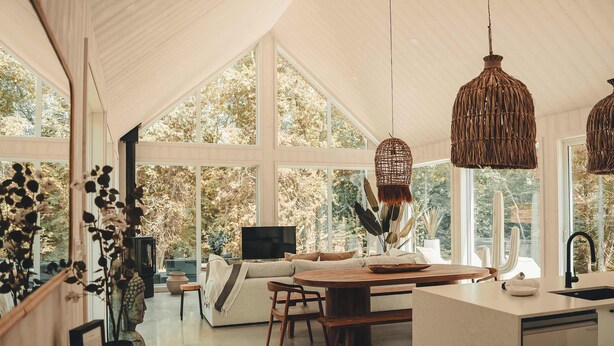 A spacious living area with a large window, a wooden dining table, and a sofa. - Two Zen Houses 4 & 7 - Villas and Spas (Morin-Heights)