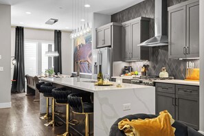 A modern kitchen with a central island, bar stools, and a dining area with a view. - Karaoke, Rooftop, Fire Pit -The Ryman (Nashville)