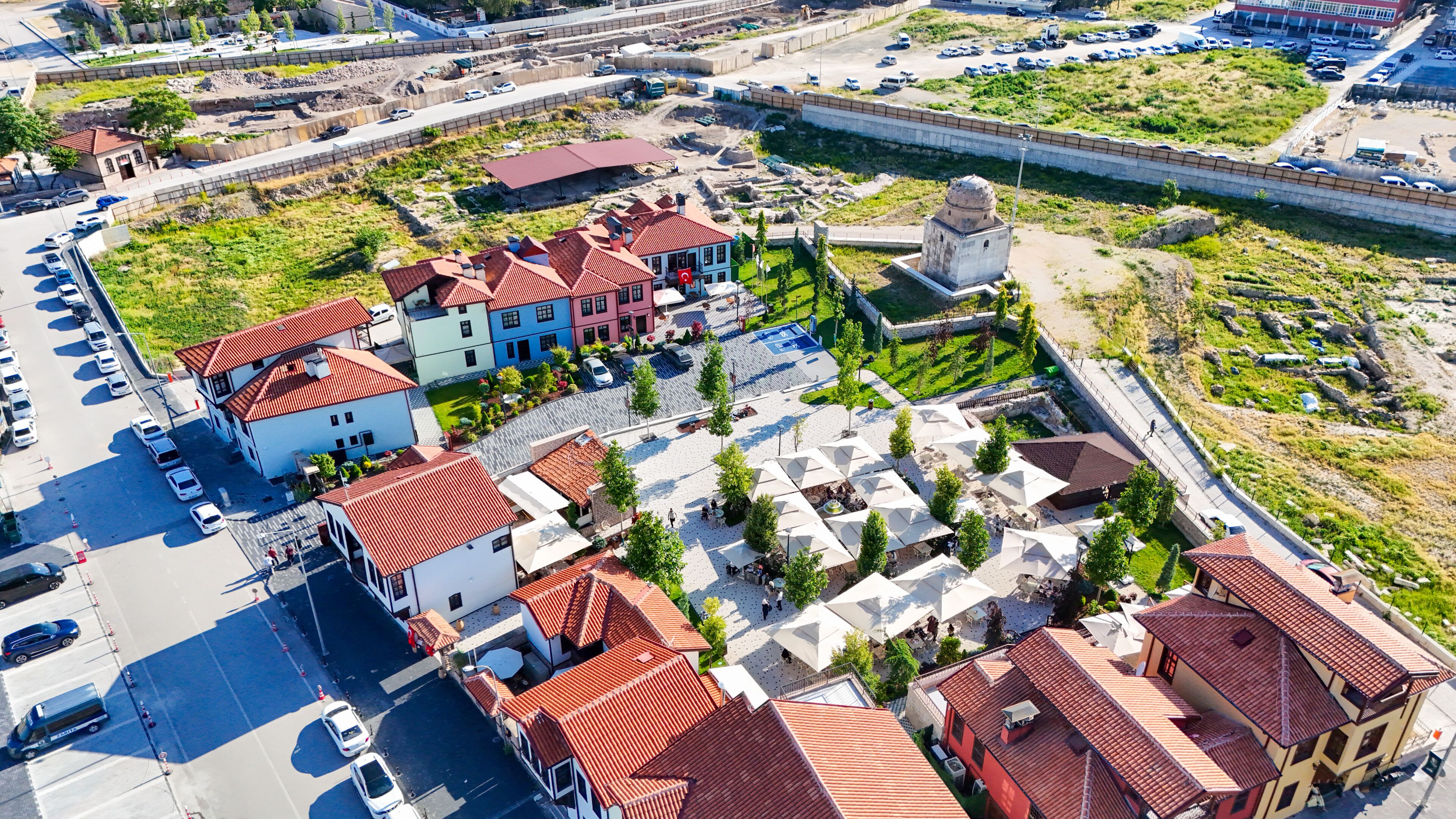 An aerial view of a town with a mix of residential buildings, a central plaza with outdoor seating, and a fortified structure.
