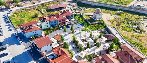 Vista aérea de un pueblo con edificios residenciales, una plaza central con mesas al aire libre y una estructura fortificada.