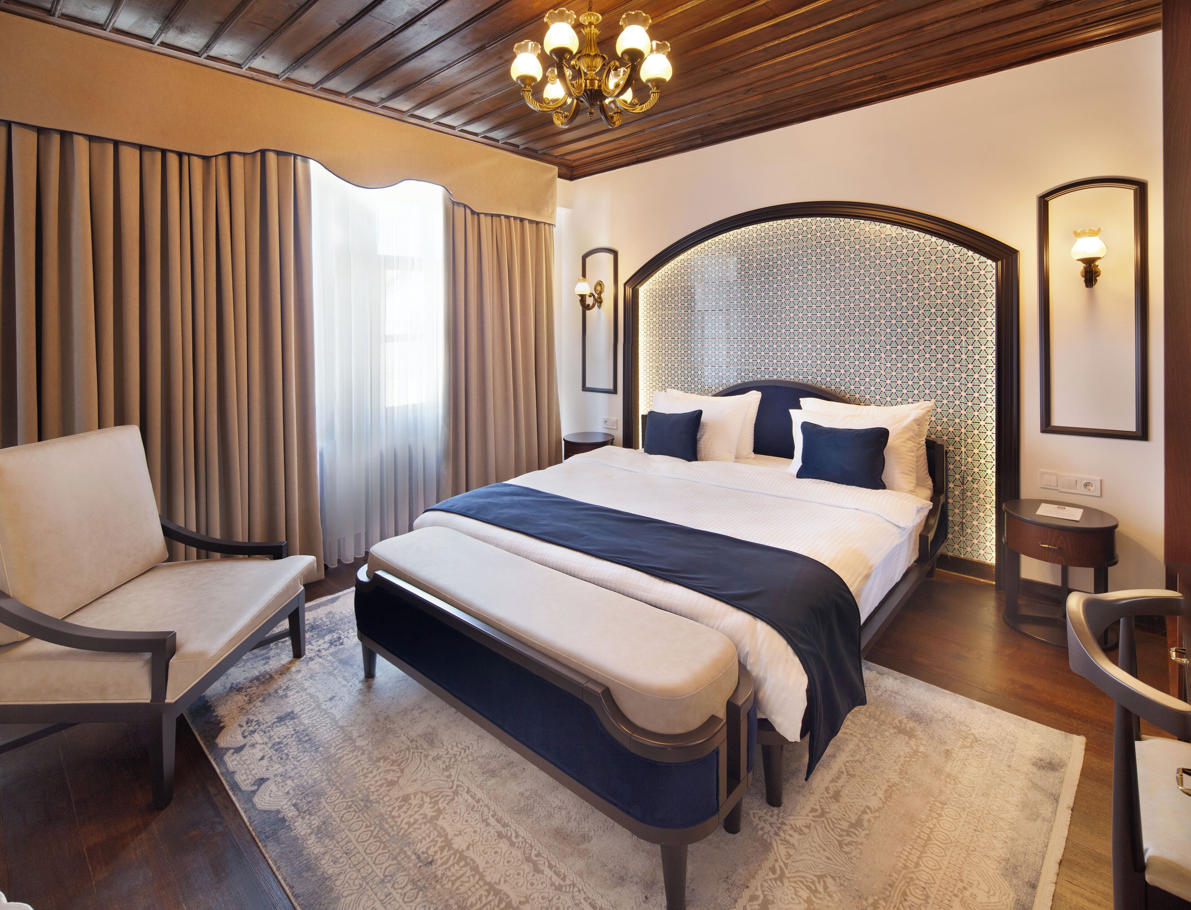 Una habitación de hotel moderna con una cama grande, un banco al pie cama, un escritorio y una silla.