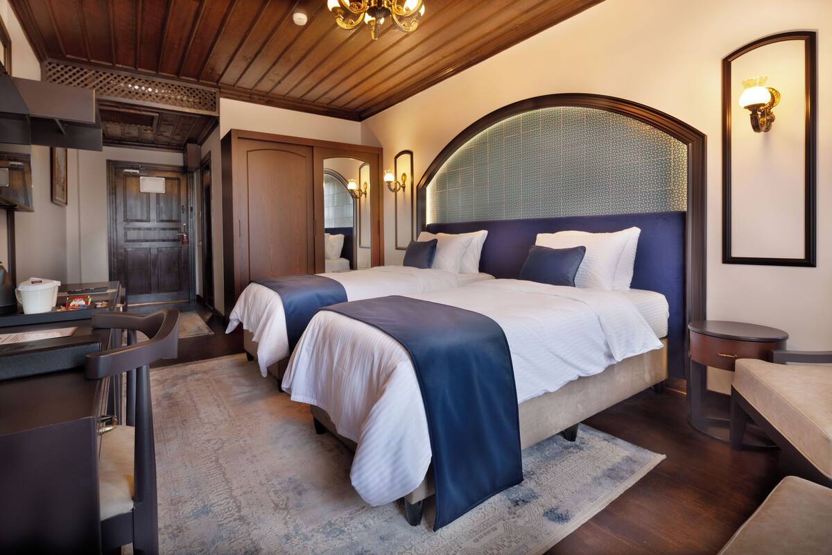 Habitación de hotel con dos camas, techo de madera, un espejo grande y un escritorio pequeño con una silla.