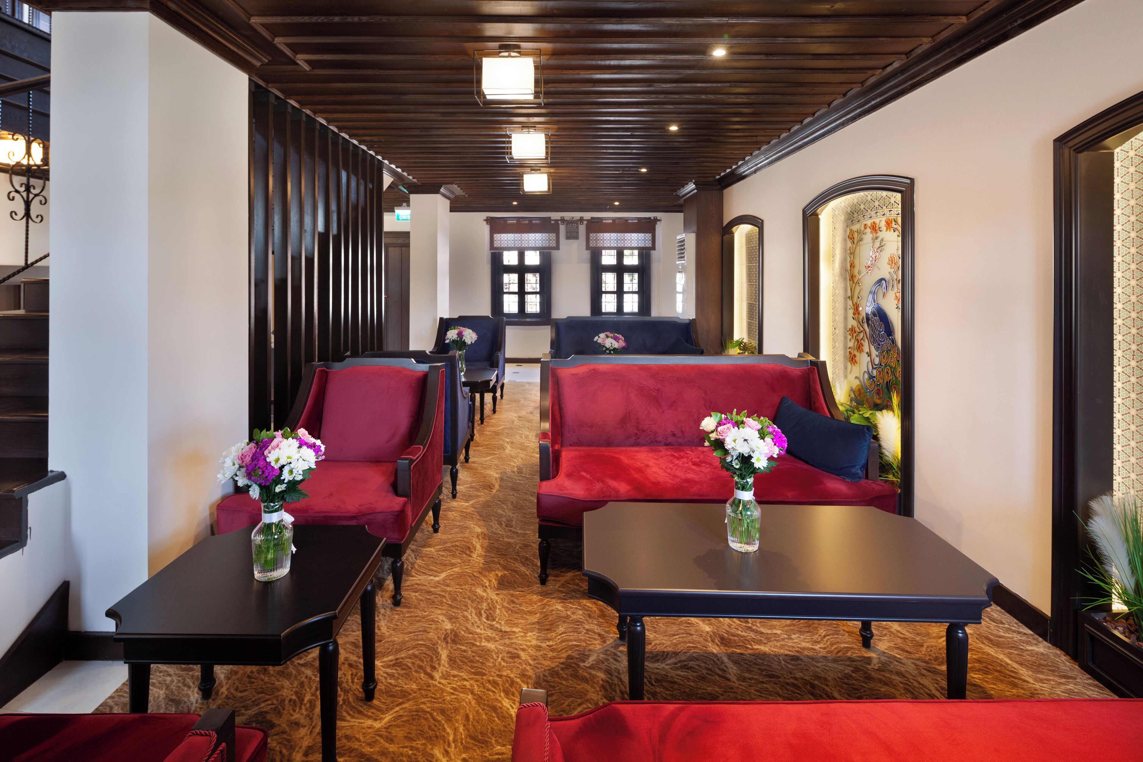 Un hall d’hôtel avec des canapés rouges, des tables noires et un plancher en bois.