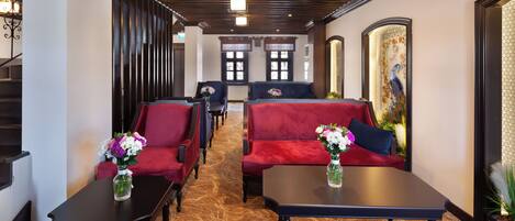 Un hall d’hôtel avec des canapés rouges, des tables noires et un plancher en bois.