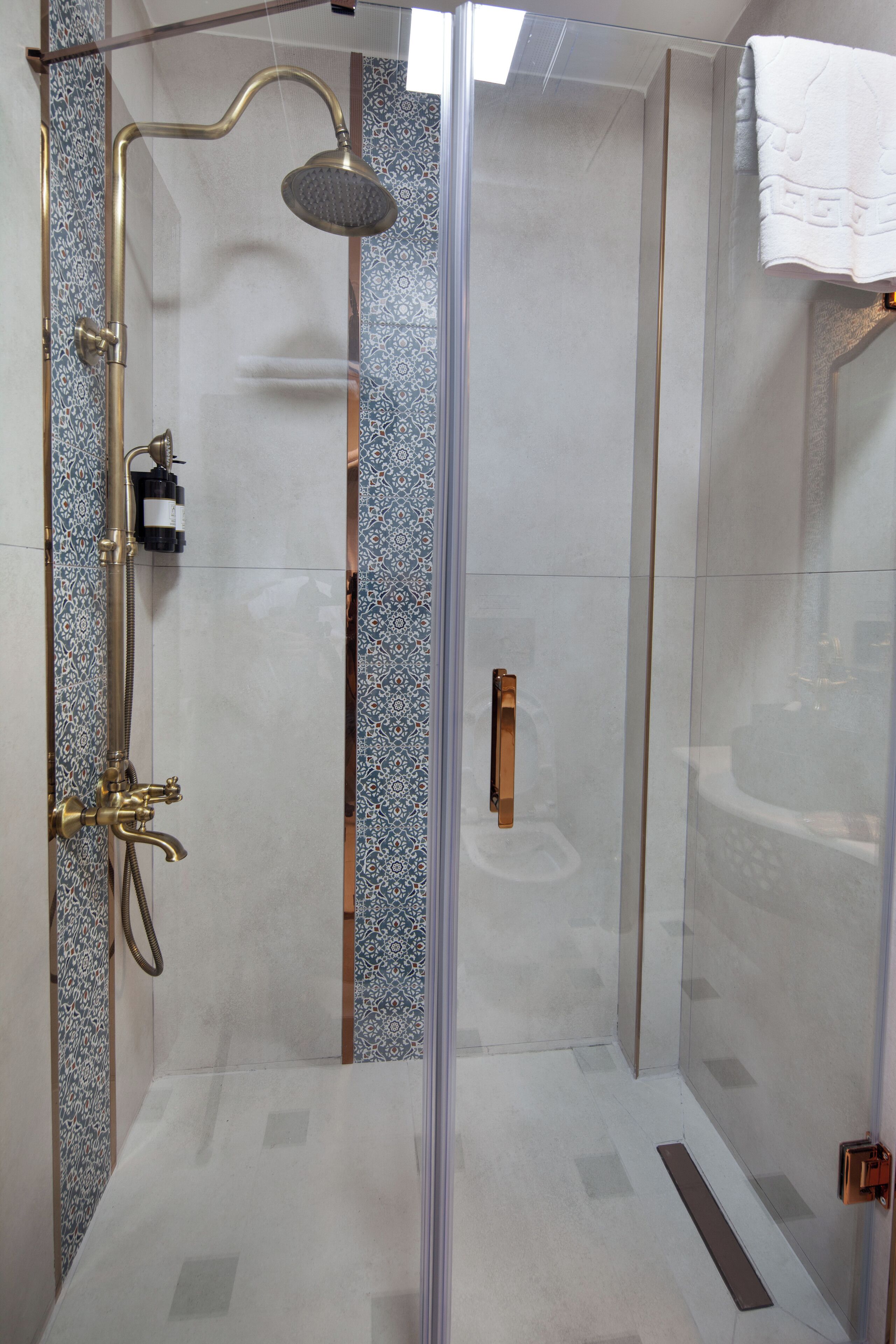 A glass-enclosed shower with a handheld showerhead and a wall-mounted faucet.