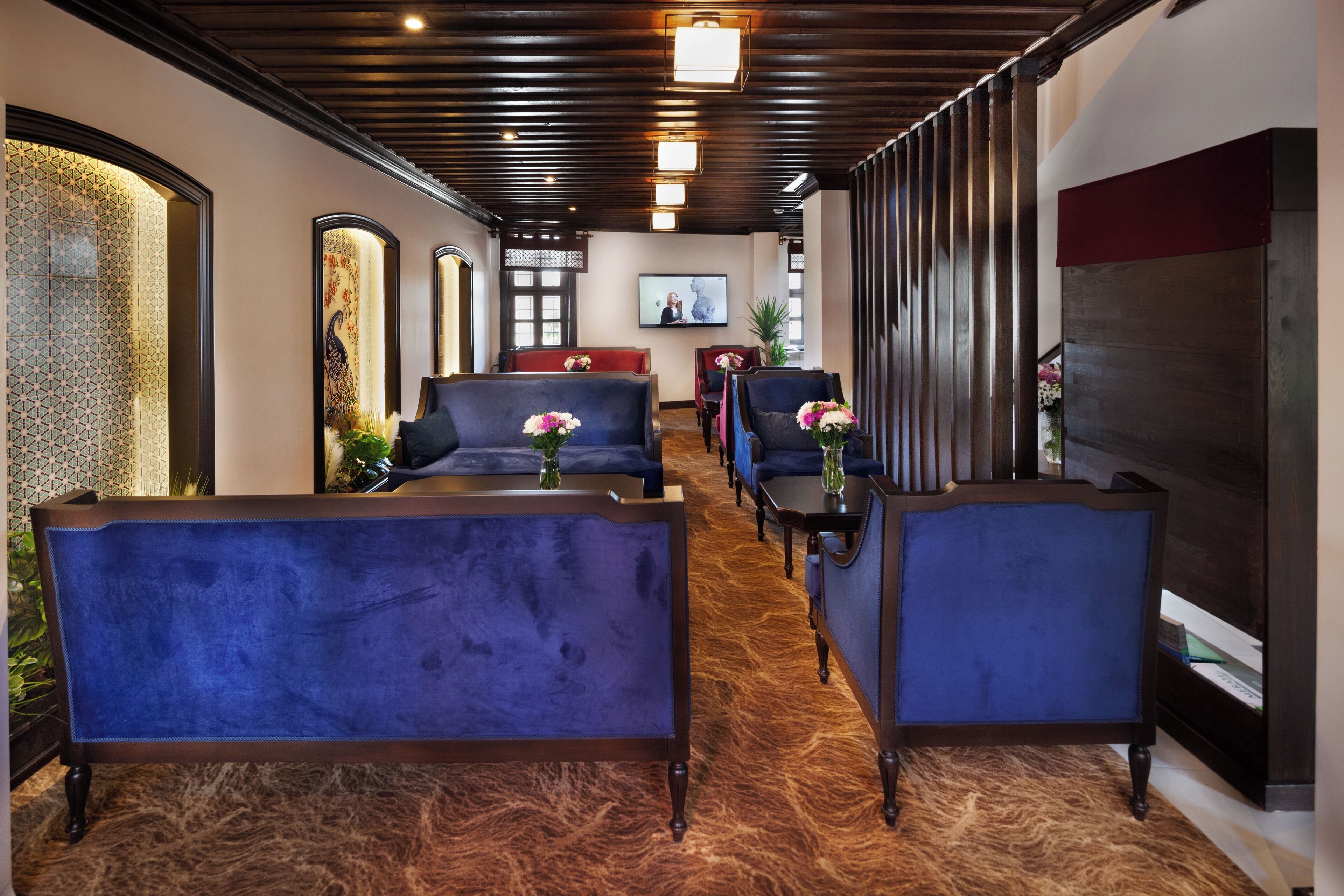 A hotel lobby with blue upholstered seating, a wooden floor, and a television on the wall.