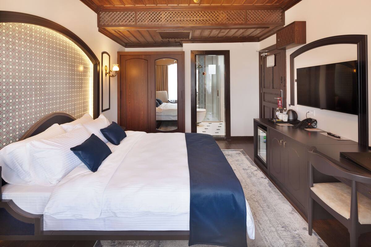 Habitación de hotel con una cama grande, un escritorio, un televisor de pantalla plana, un espejo y un armario.