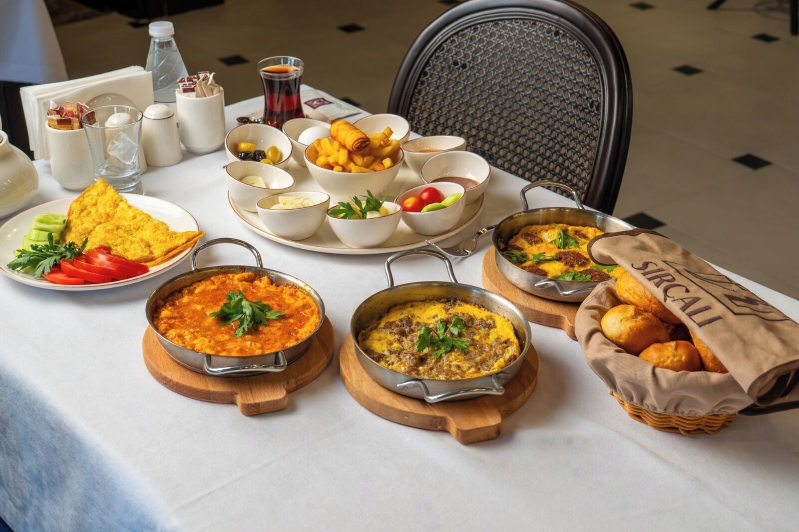 A table set with various dishes, including a bowl of soup, a plate of fries, and a basket of bread.