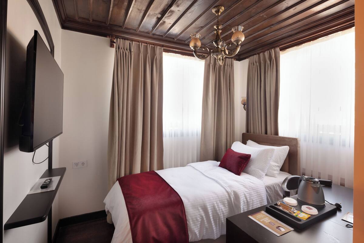 Habitación de hotel con cama, televisión, escritorio y tetera, además de cortinas.