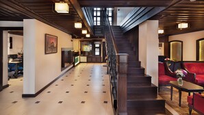 A spacious hallway with a wooden staircase leading to a second floor, a reception desk, and a seating area with red chairs. - SIRÇALI HOTEL (Konya)