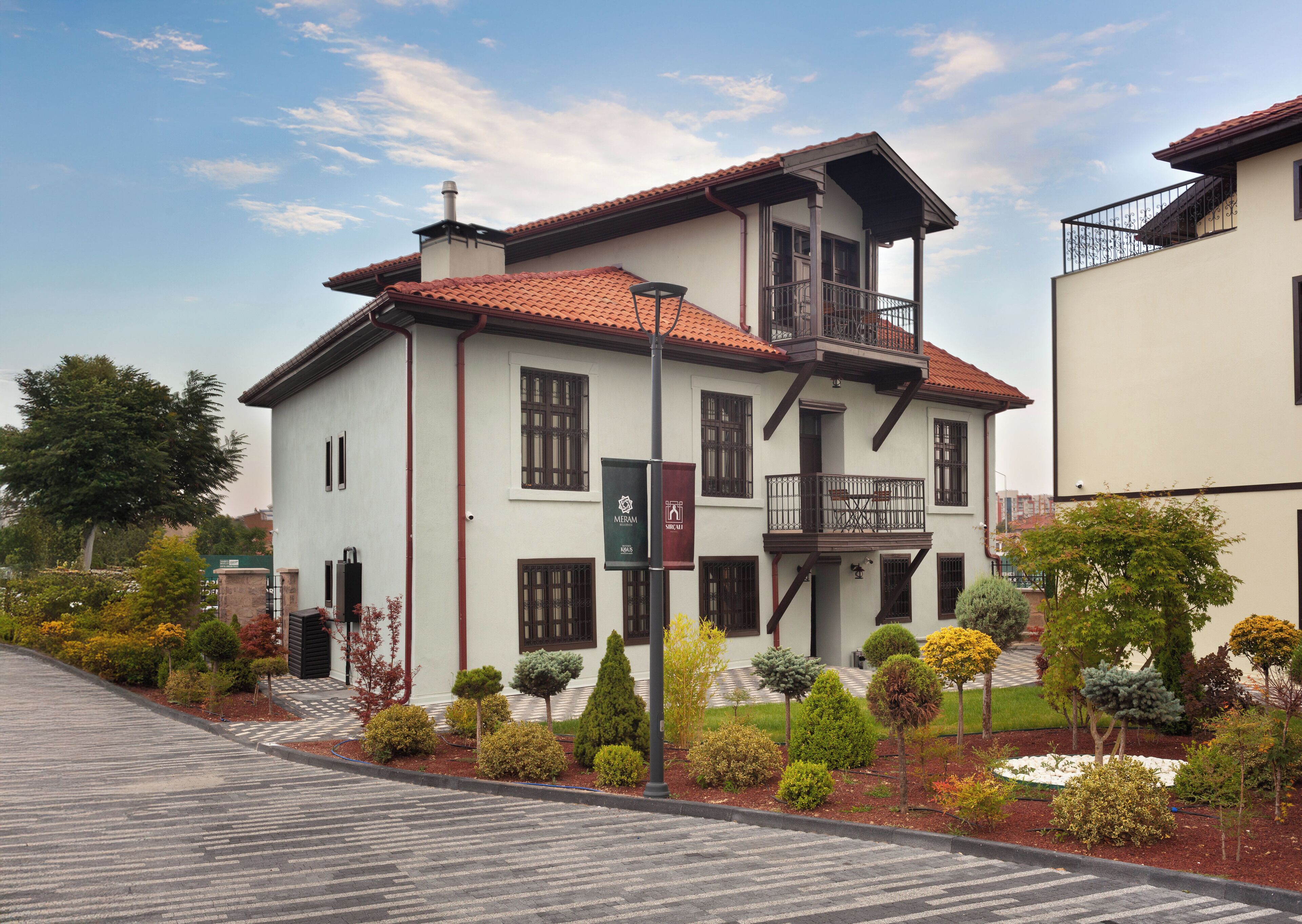 A two-story building with a balcony, surrounded by well-maintained gardens and a paved driveway.