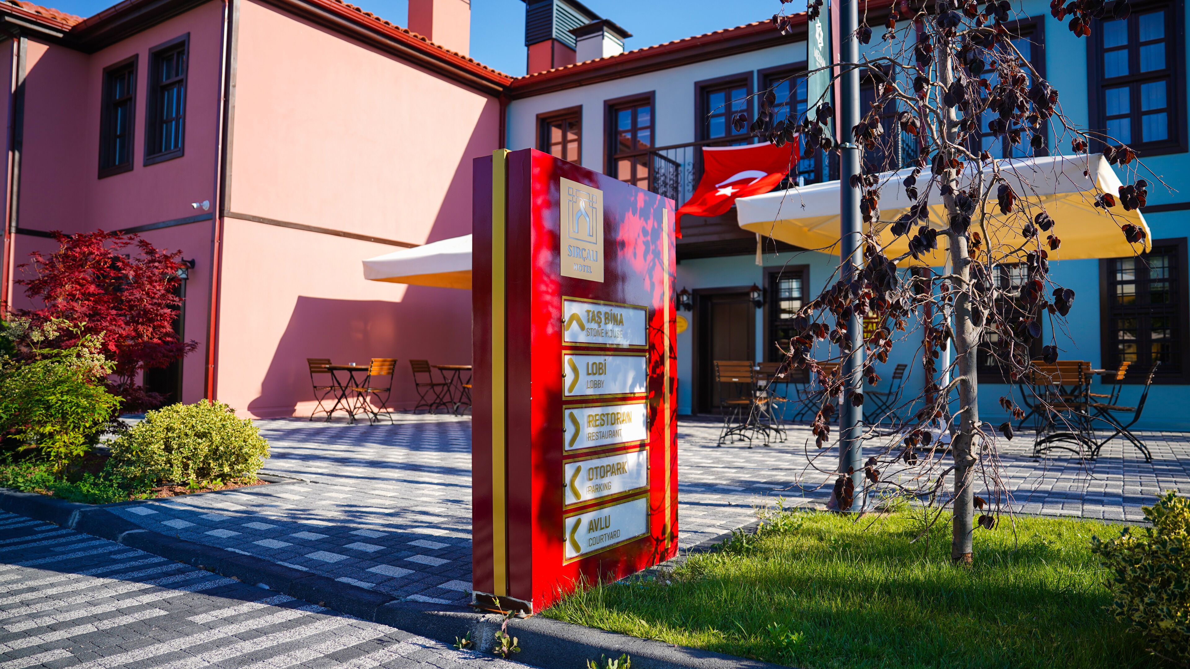 Entrada de hotel con letreros indicativos, asientos al aire libre y fachada del edificio.