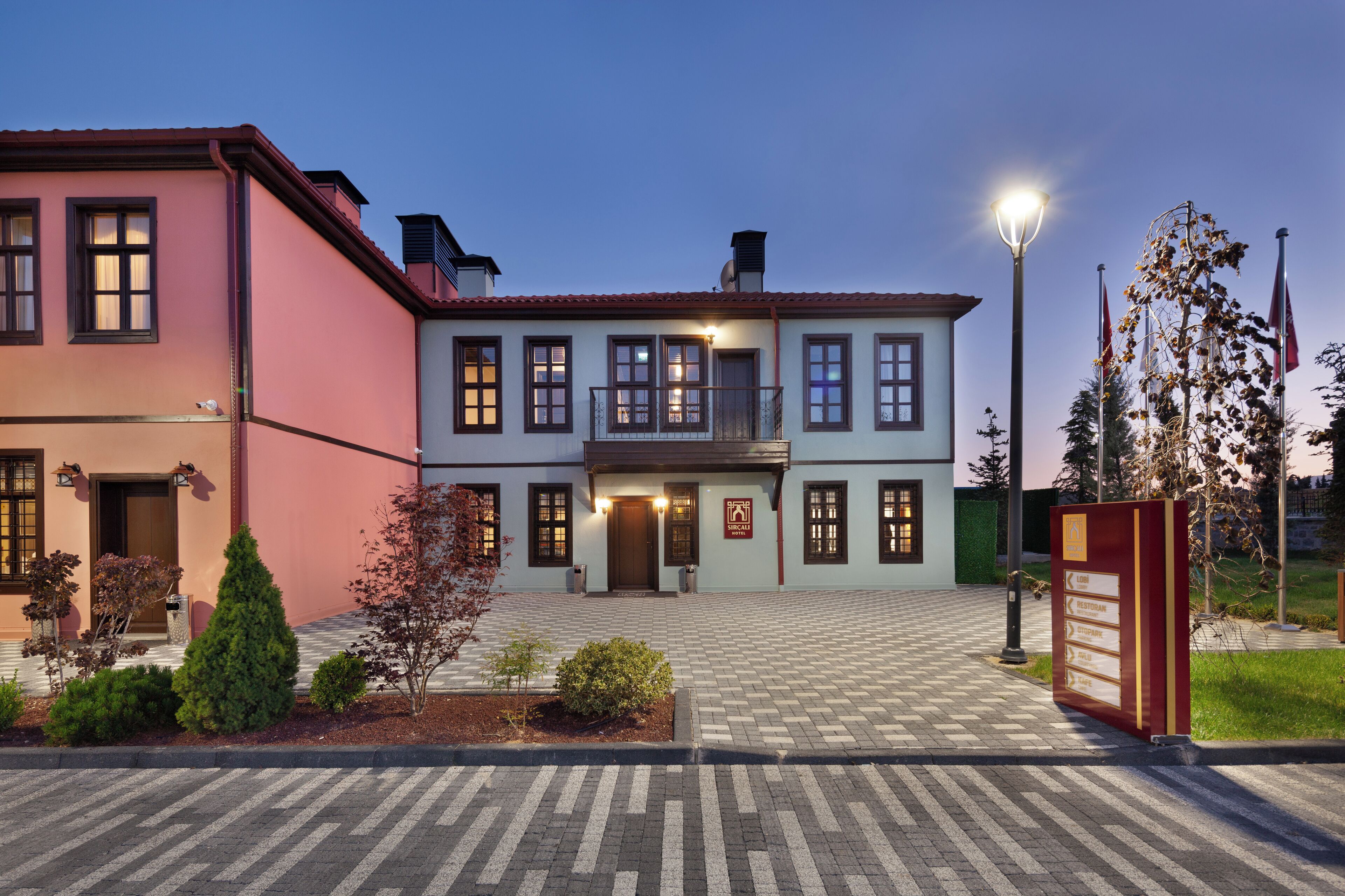 A two-story building with a red and white facade, a central entrance, and a landscaped front yard with shrubs and a small tree.