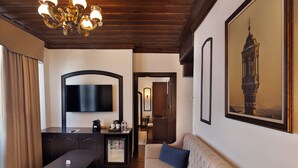 A hotel room with a wooden ceiling, a sofa, a dining table, a minibar, a TV, and a large framed picture on the wall. - SIRÇALI HOTEL (Konya)