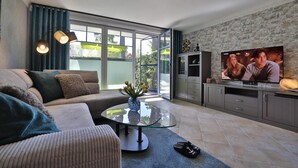Un salon moderne avec un canapé, une table basse en verre, un téléviseur et une vue sur l’extérieur.