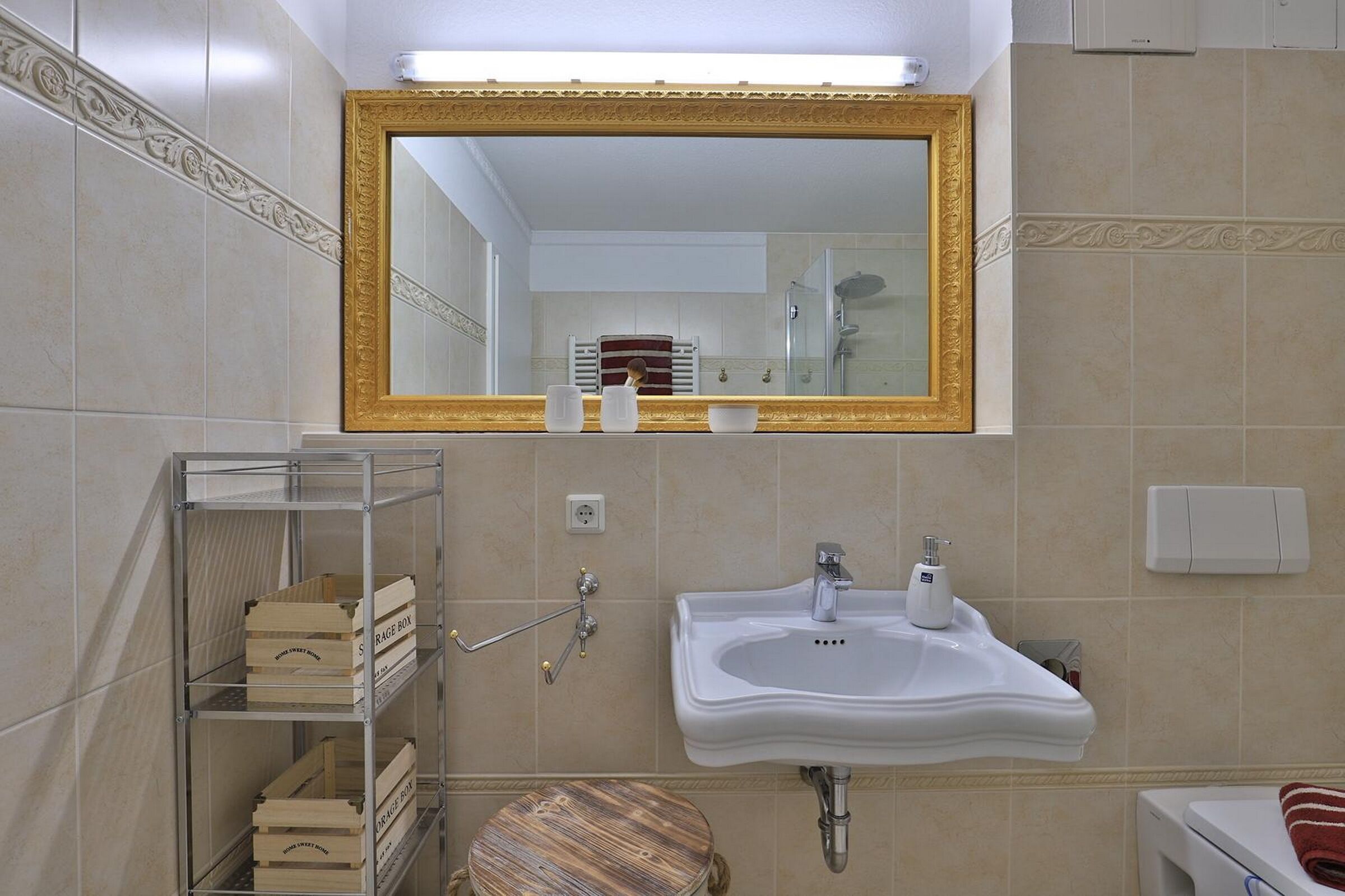 A bathroom with a large mirror, a sink, a toilet, and a shelf with storage boxes.