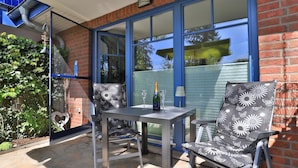 Une terrasse avec une table et deux chaises, une bouteille de champagne et un verre.