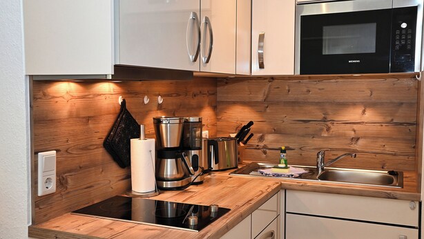 Eine moderne Küche mit Holzelementen, einer eingebauten Mikrowelle und einem Spülbecken.