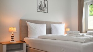 Ein ordentlich bezogenes Bett mit weißen Bettwäsche, ein Nachttisch mit Lampe und ein gerahmtes Kunstwerk an der Wand.