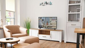Ein modernes Wohnzimmer mit einem beigefarbenen Sofa, einem kleinen runden Tisch und einem Flachbildfernseher an einem Holzkasten.