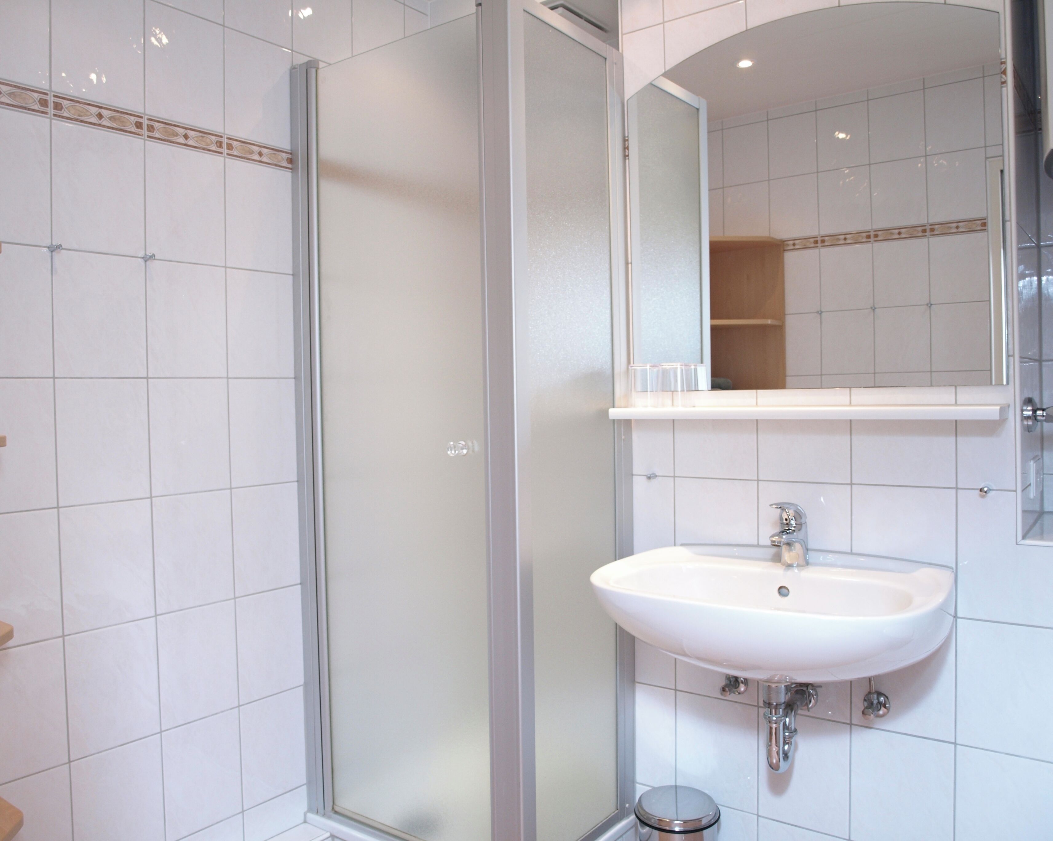 Une salle de bain avec une douche à parois de verre, un lavabo blanc et un miroir au-dessus du lavabo.