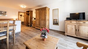 Une pièce avec une table à manger en bois, un téléviseur posé sur un meuble et un miroir au mur.