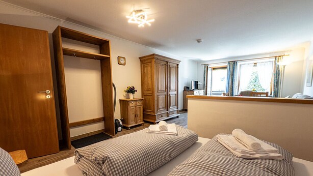 Une chambre d’hôtel avec deux lits, une armoire, un miroir, une fenêtre avec des rideaux et une horloge au mur.