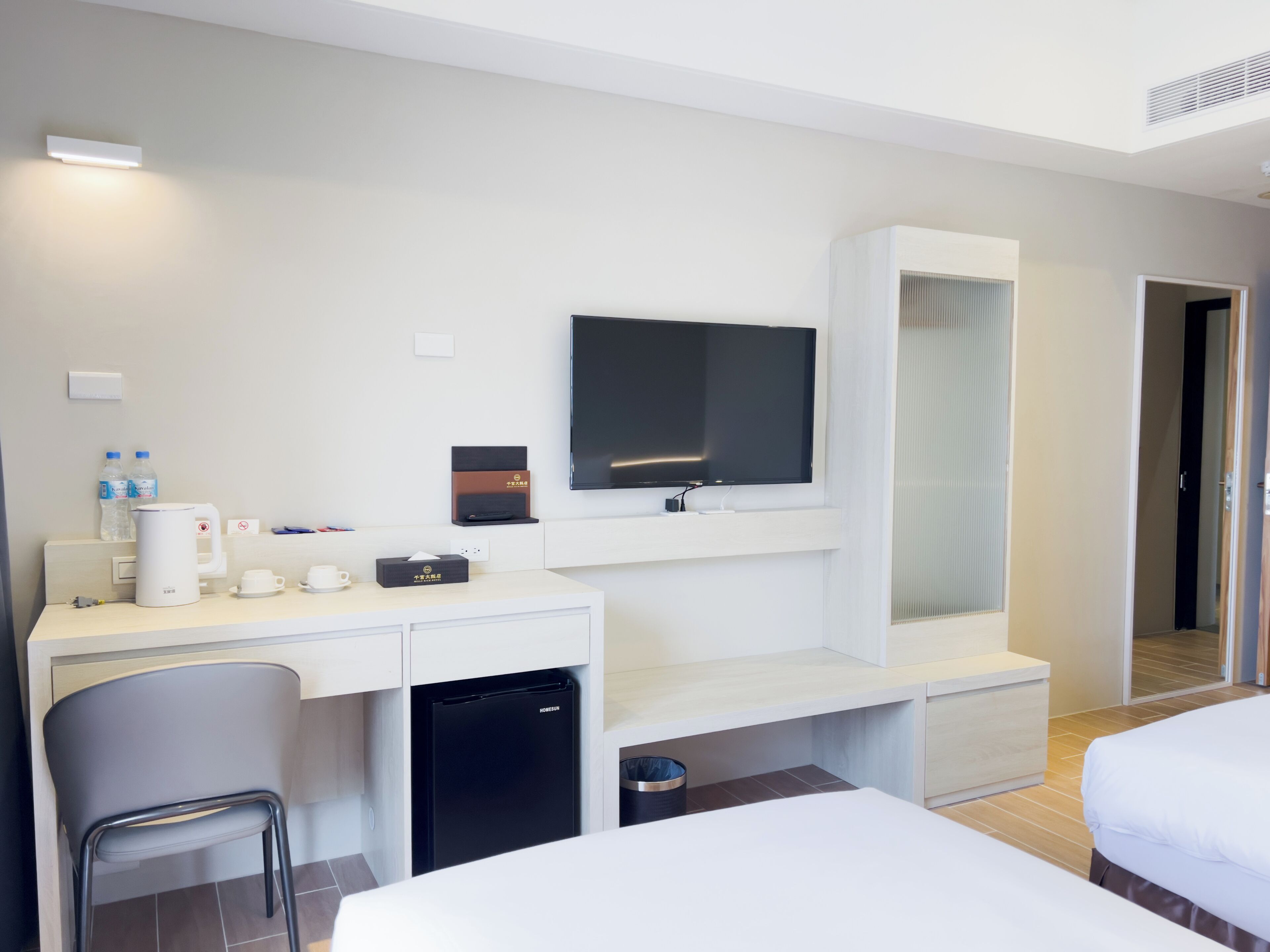 A hotel room with a bed, a desk with a television, a mini-fridge, a chair, and a minibar.