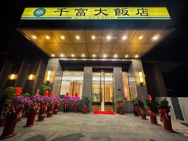 Exterior del hotel Mille Rich, con una entrada destacada, plantas en macetas y señalización iluminada.