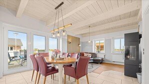 A spacious dining area with a wooden table and red chairs, a modern kitchen with a built-in stove, and large windows offering views of the outside. - Vacation home Marga Sophie- dreamlike idyll under thatch in Dagebüll (Dagebüll)