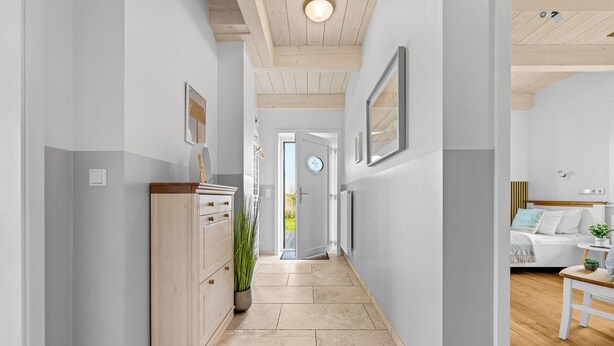 A hallway with a wooden cabinet, a potted plant, and a door leading to a room with a bed and a small table. - Vacation home Marga Sophie- dreamlike idyll under thatch in Dagebüll (Dagebüll)