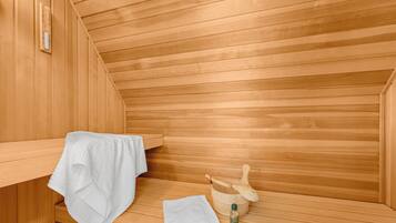 A sauna room with wooden walls, a bench, a towel, a wooden bucket, and a bottle of oil.
