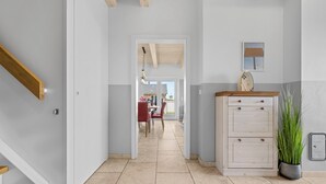 A hallway with a wooden staircase, a dining area with red chairs, a white cabinet with drawers, and a potted plant. - Vacation home Marga Sophie- dreamlike idyll under thatch in Dagebüll (Dagebüll)