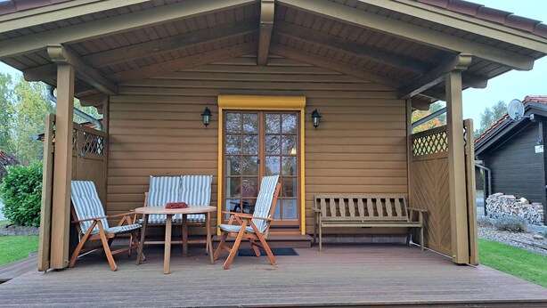 A wooden cabin with a porch, two striped chairs, a bench, and a table.